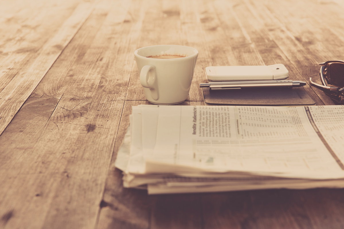 Zeitung, Kaffeetasse und Handy liegen auf einem Tisch